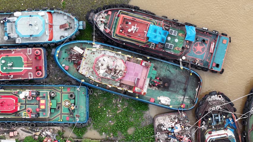 A tugboat parked on the edge of the river, a tugboat moored behind a housing complex near the river