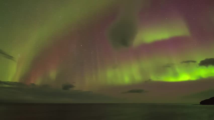 Vibrant green and red aurora borealis lights illuminate the night sky above a tranquil ocean, reflecting the celestial display