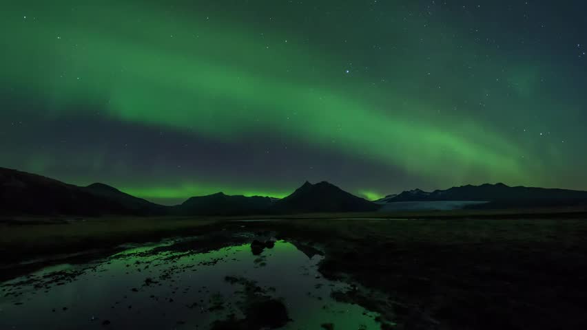 Experience the breathtaking spectacle of the Northern Lights illuminating the night sky above a rugged mountain landscape with a serene water reflection