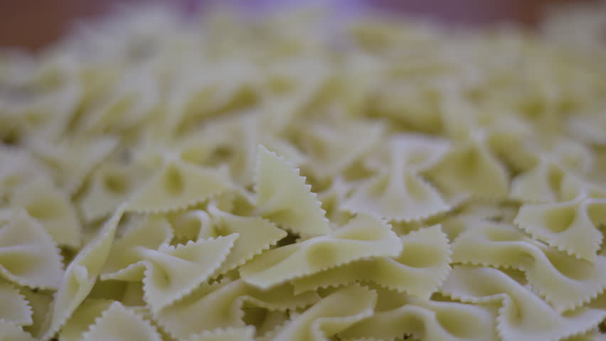 Uncooked Bow Tie Pasta On Table Dry. Close up of farfalle macaroni dropping into a ceramic bowl, suitable for italian food commercials or cooking tutorial videos.