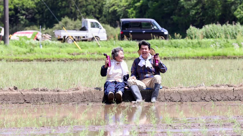 A senior couple rehydrates during a break from rice planting.