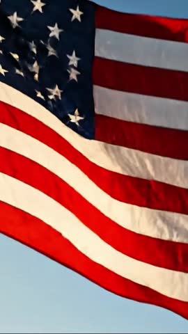 Close-up of the American flag waving slowly against a clear blue sky, patriotic USA banner fluttering in sunlight, symbol of freedom