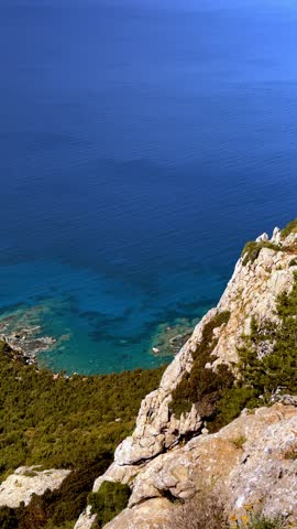 Scenic vertical drone view of Fountain Amoros coast with steep rocky cliffs descending into transparent blue sea, showcasing pristine wilderness and tranquil beauty.