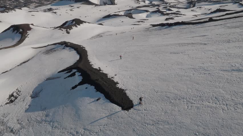 Aerial view of hikers trekking across the snow-covered volcanic ridges near Rifugio Sapienza on Mount Etna in Nicolosi, Sicilia, Italy.