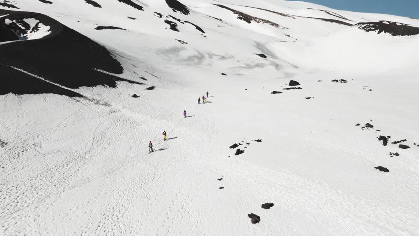 Aerial view of hikers trekking in a line across the vast snow-covered volcanic landscape near Rifugio Sapienza in Nicolosi, Sicilia, Italy.