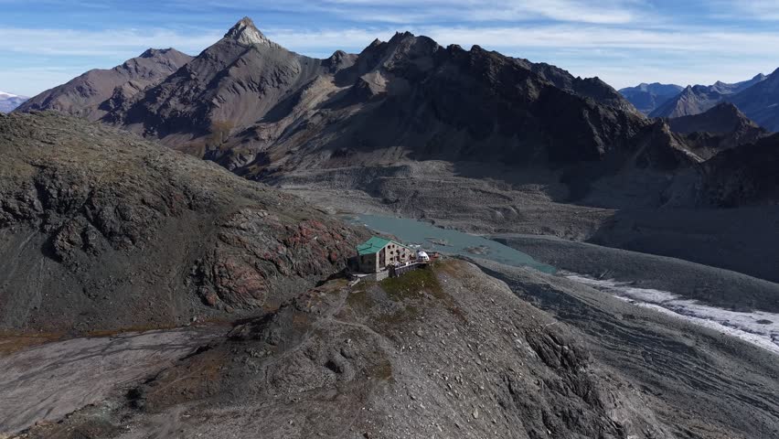 Aerial flyover of a mountain hut alongside Glacier de Cheilon as the morning sun shines over the mountain peaks of Swiss Alps in the Arolla region and Dixence valley