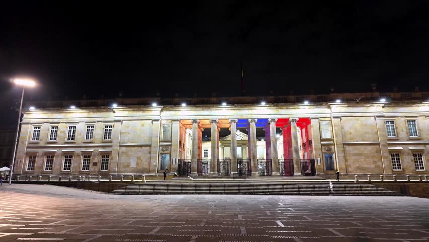 Exterior view of the illuminated neoclassical building housing the Congress of Colombia during a quiet evening in the capital.