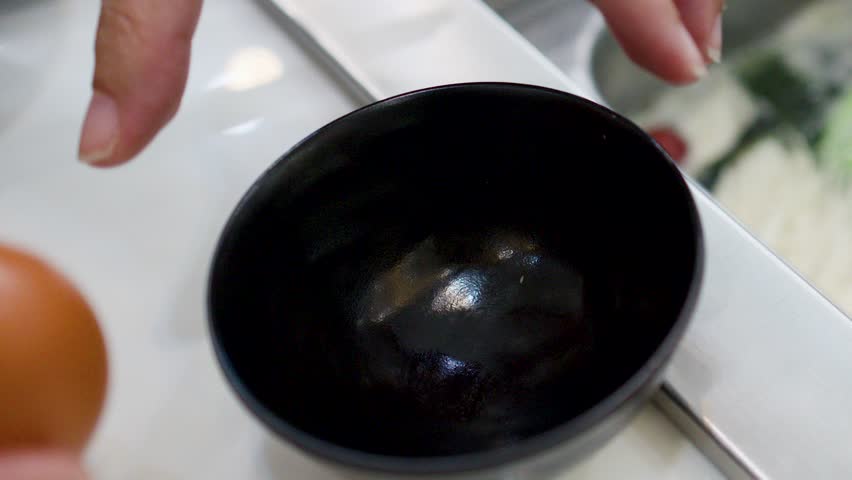 A person cracks a fresh egg into a black bowl for Japanese shabu shabu cooking