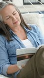 Vertical video: Settling woman reading paperback on porch hammock, touching hair in denim, to relax. Balcony, reader, book, lifestyle, outdoor, cushion, vertical video - Powered by Shutterstock - Get 15% off with code: PIKWIZARD15