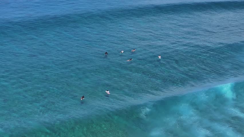 Aerial view of surfers floating in the clear blue ocean as large waves roll in Thulusdhoo, Kaafu Atoll, Maldives.