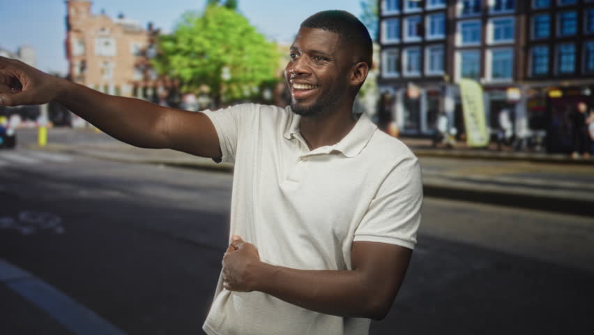 Young man points with outstretched arm while clutching stomach and showing stomachache on a busy urban street lined with buildings and cafes; concern urgency.