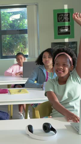 Vertical video: Front student raising hand, speaking in class after teacher cue with laptop headset. Classroom, participation, interaction, learning, engagement, collaboration, vertical video