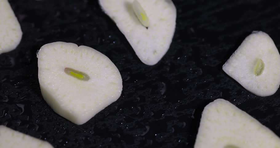 freshly peeled and sliced garlic cloves scattered on black slate, peeled and sliced fragrant and fresh spices from garlic cloves scattered on black slate stone, covered with drops of water