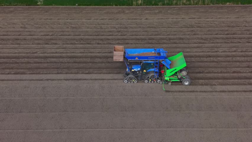 Aerial view of a blue tractor with a green attachment planting seeds in a brown agricultural field with parallel furrows Middenbeemster, North Holland, Netherlands.