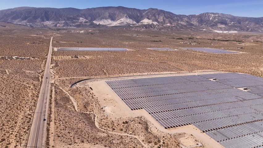 Aerial view of vast solar panel arrays situated in a dry desert landscape next to a long straight road with mountains in the distance Lucerne Valley, California, United States.