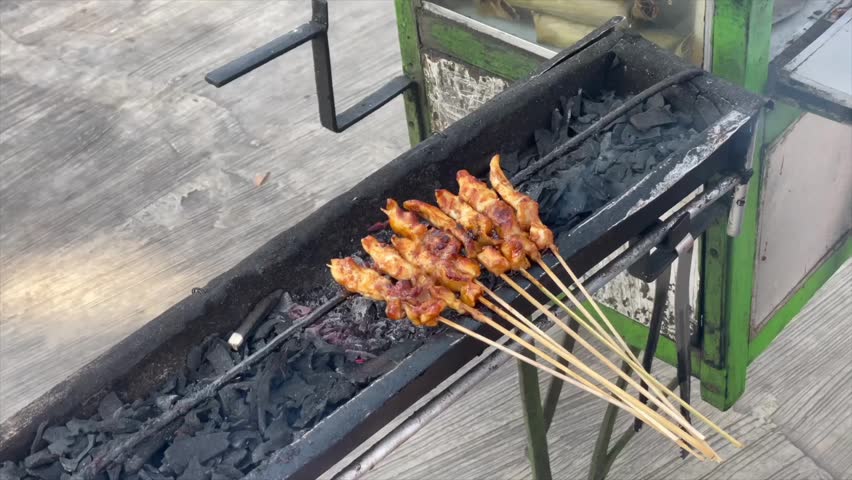 Traditional indonesian chicken satay being grilled over charcoal on a street food cart.