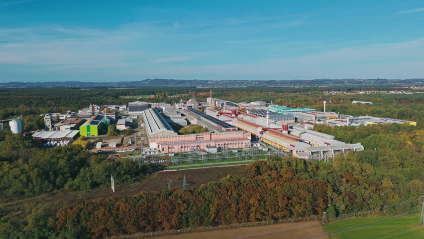 Aerial view shows a large aluminum factory and industrial complex surrounded by fields and trees, revealing metal production facilities.