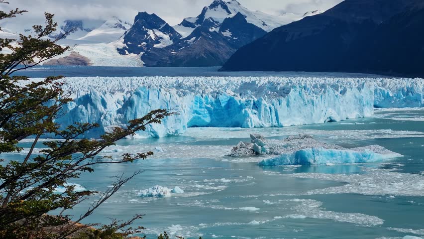 Picturesque view of the impressive Perito Moreno Glacier in Argentina, its towering white and blue ice wall rising above Lago Argentino, with snow covered Andes peaks forming a dramatic backdrop