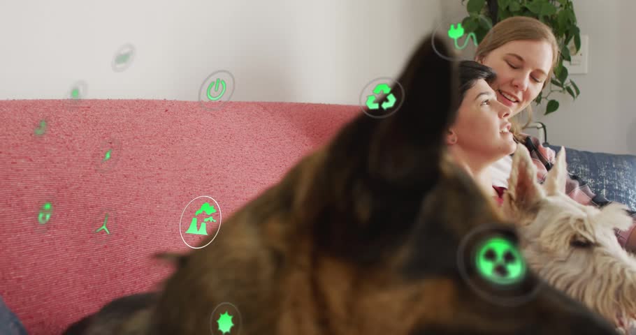 Dog shifting foreground two women leaning smiling as animated green icons float across for eco ad. Canine, couple, couch, cushions, livingroom, affection, relaxation
