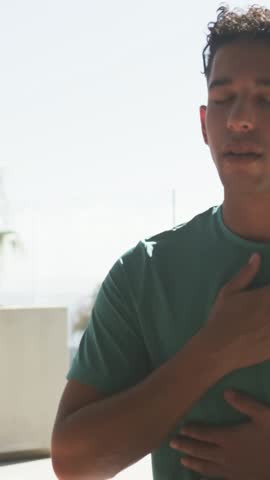 Vertical video: Breathing man teal, opening eyes smiling as sun calming on balcony palm, copy space. Terrace, outdoor, backlit, relaxed, horizon, green, vertical video