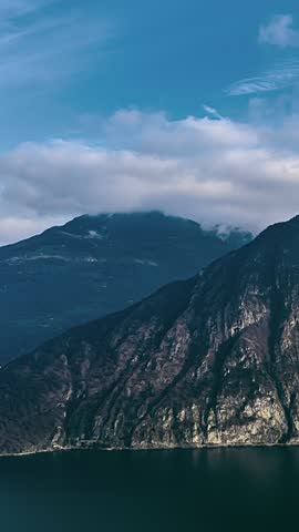 Clouds drift over rugged mountains above a tranquil lake in natural daylight