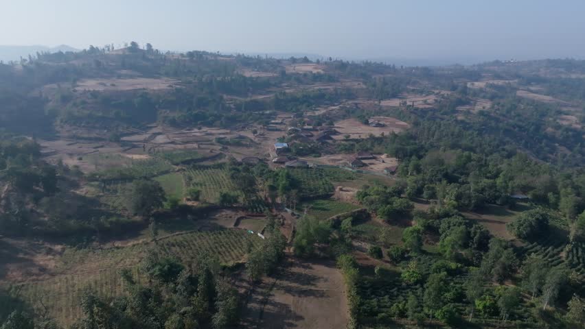 Remote village settlement in Vansda, Gujarat, India, showing scattered houses and agricultural plots across hilly terrain. Slow forward drone shot moving closer to the rural traditional houses.