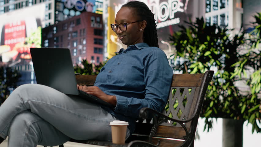 Student drinking coffee on park bench, using laptop to do homework and study course materials. Woman enjoying caffeinated beverage outdoors in the morning, using notebook to prepare assignment.