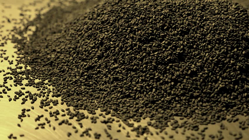 A pile of black sesame seeds spilled on a reflective surface, creating textured background