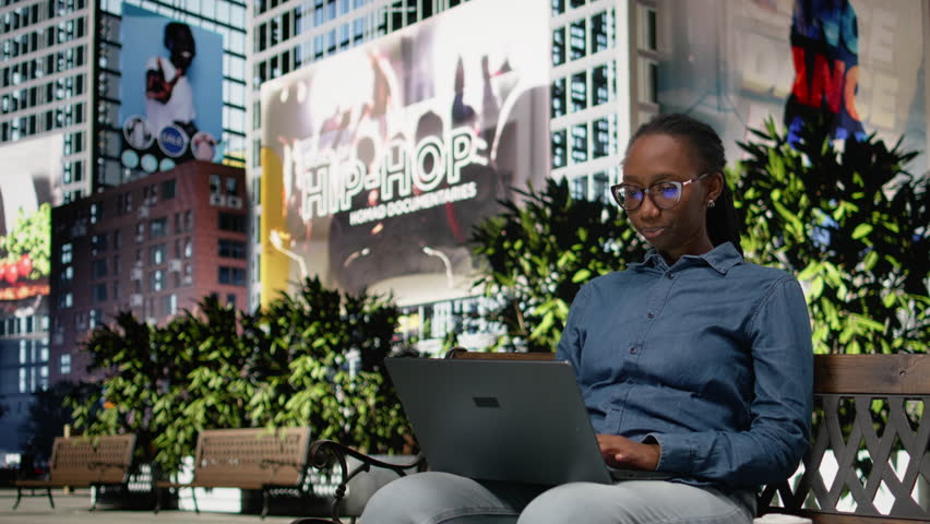 Stressed woman feeling burnout while using laptop on park bench, struggling to solve business tasks. Black girl unhappy and worried with deadline approaching, trying to relax outside.