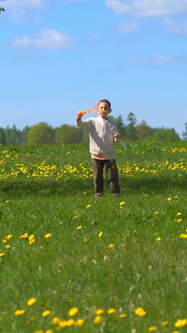 Young Boy Blowing Large Soap Bubbles in Dandelion Field, Child Playing in Sunny Spring Meadow, Happy Childhood Outdoor Activity in Nature Vertical