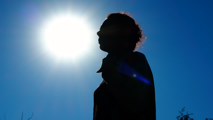 Woman drinking water under the sun silhouette. Silhouetted female standing against bright sky, drinking water while battling intense summer heat and seeking refreshment from scorching sunlight