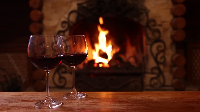 Glasses of red wine on wooden table near fireplace at home
