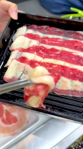 A person uses metal tongs to dip thin beef slices into boiling broth at dinner