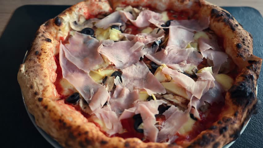 Italian pizza capricciosa close up with ham mushrooms olives artichokes and crispy crust in motion.