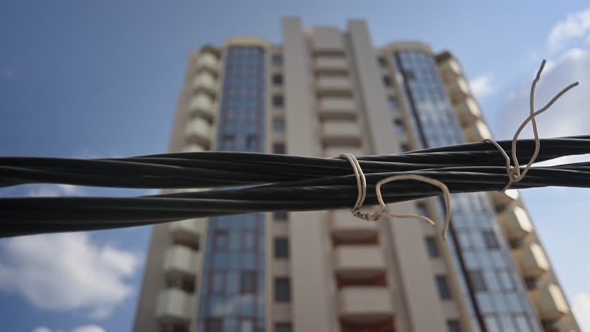Modern apartment building rising against sky with focus on twisted wires.