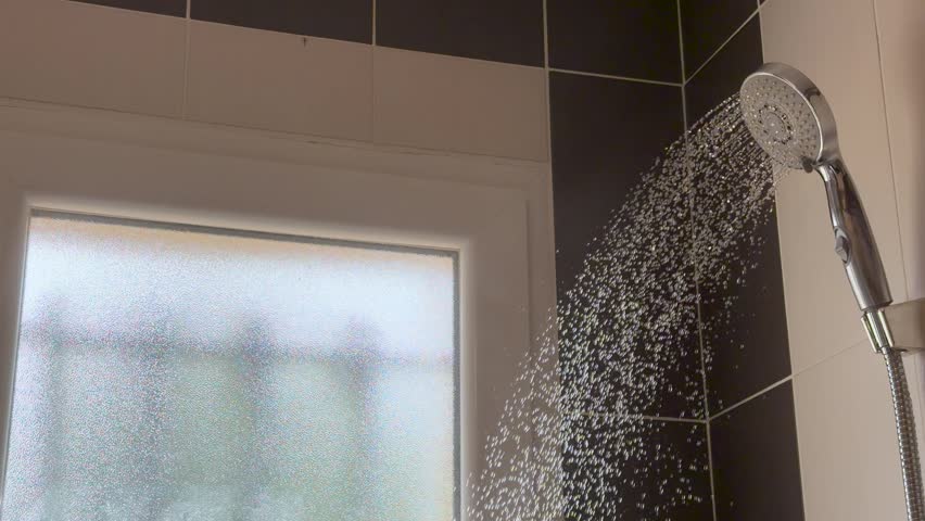 Hot water sprays from a chrome shower head against beige tiles in a steamy bathroom