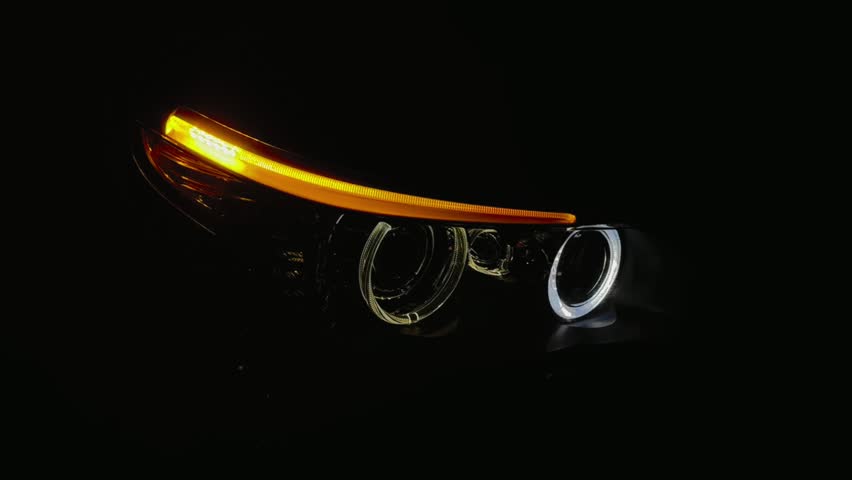 BI-LED headlights of a modern and expensive black car, hood and radiator grille. Front BI-LED headlight on a black sedan car. Glossy black premium car BI-LED headlights close-up. Angel eyes headlight.