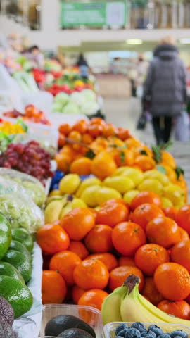 Vibrant assortment of fresh fruits arranged in rows at market stall. Oranges, apples, bananas, avocados and other produce at local farmer market. Blurred people walking at background