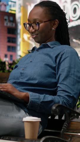 Vertical Video Student drinking coffee on park bench, using laptop to do homework and study course materials. Woman enjoying caffeinated beverage outdoors in the morning, using notebook to prepare