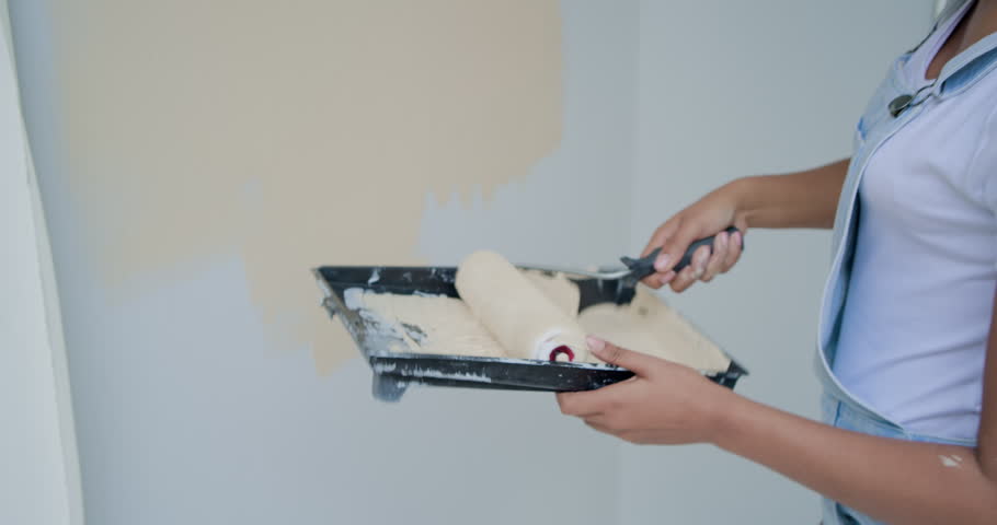 African American woman painting entry patch with roller and tray to cover bell, vent, copy space. Painter, diy, toolbox, ladder, dropcloth, beige, neutral