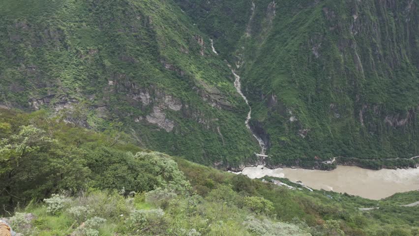A cinematic aerial perspective of the deep Tiger Leaping Gorge canyon featuring the rushing Jinsha River and lush mountain slopes in Yunnan, China.