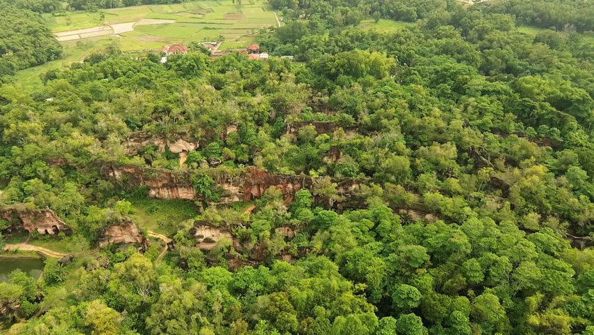 Aerial cinematic view of Arosbaya limestone hill with unique hand-carved patterns and caves in Madura, Indonesia.