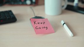 A sticky note with the message Keep Going sits on a desk next to a pen and a mug. - Powered by Shutterstock - Get 15% off with code: PIKWIZARD15
