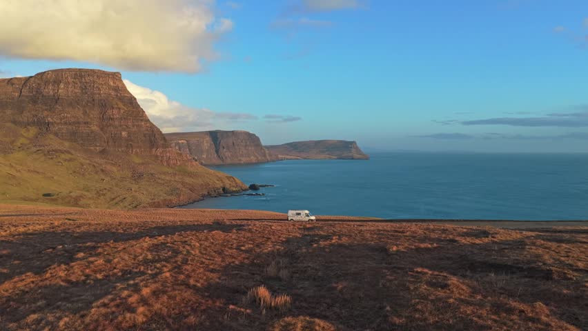 Beautiful aerial view of a motorhome traveling along a winding road on the isle of skye, with dramatic cliffs and the ocean at sunset