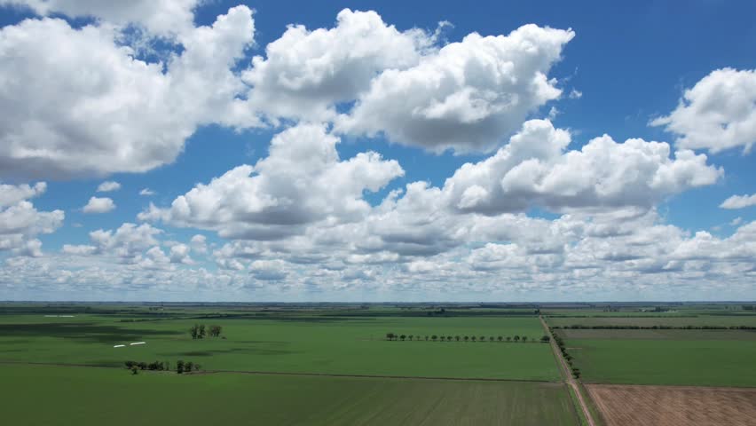 High quality aerial timelapse showing cumulus and stratocumulus clouds changing shape and moving over vast green agricultural fields with fast shadows in the Santa Fe pampas region