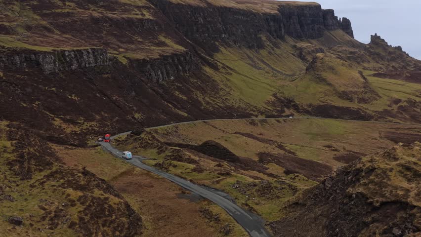 Aerial view of cars driving along a narrow road that twists through the dramatic landscape of the quiraing on the isle of skye, scotland