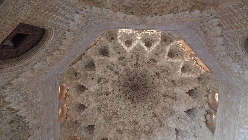 Intricate muqarnas ceiling in Alhambra palace, showcasing ornate Islamic architecture, carved stucco, star-shaped vaulting and warm light filtering through arched windows in historic interior, Granada