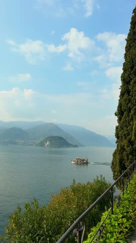 Scenic view of Lake Como with a ferry boat cruising towards Bellagio peninsula under a blue sky with soft white clouds in Italy.