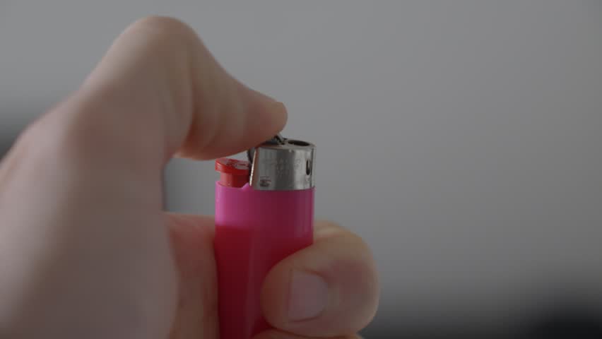 Lighting up a flint-wheel lighter with his thumb while holding it in his hand, closeup