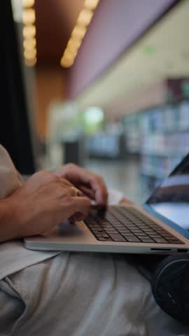 Vertical Close-Up View Of Person Using Laptop Inside Library Environment, Modern Technology, Remote Work, and Studying in Educational Space
